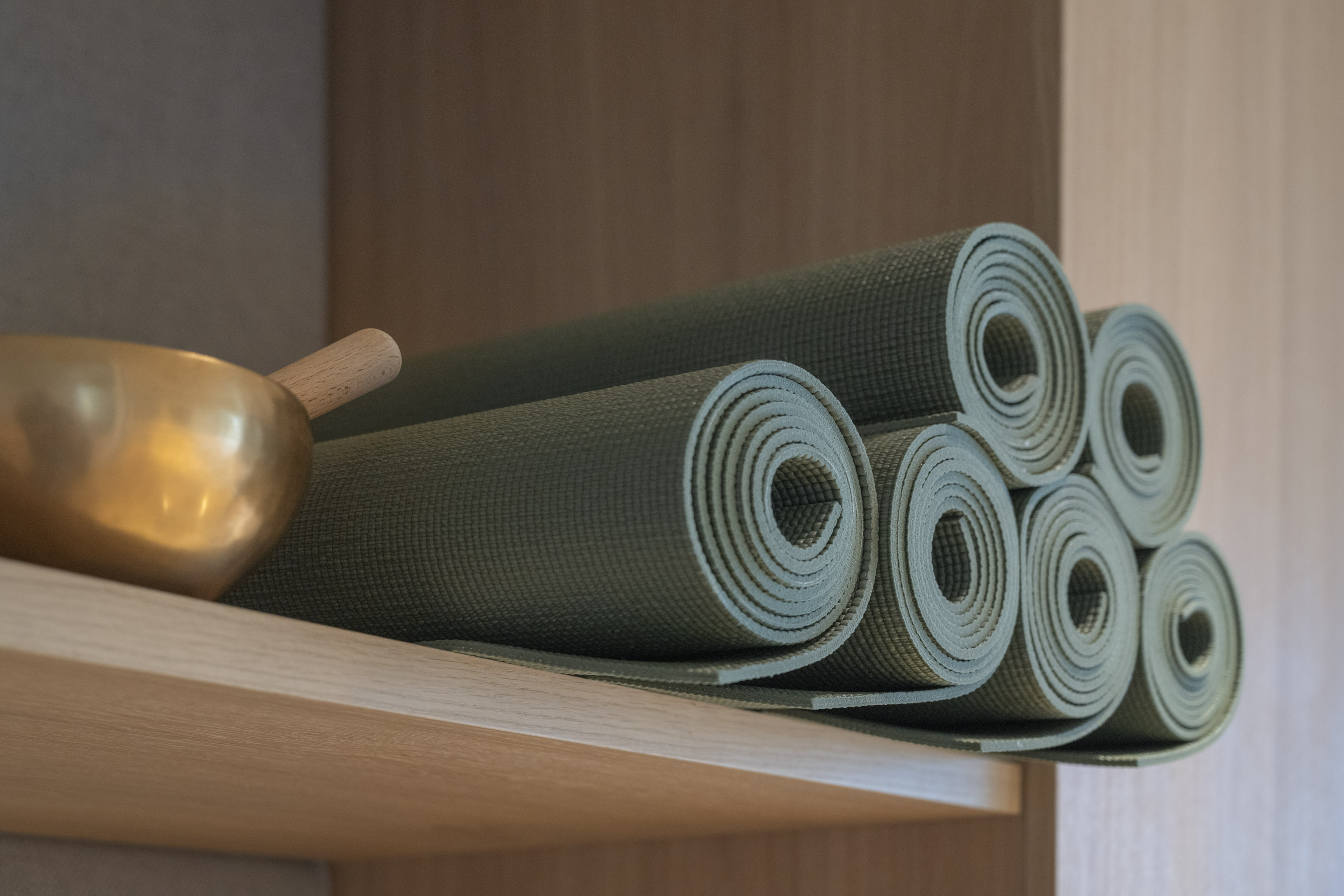 Gerollte Yogamatten und Klangschale auf einem Holzregal im Yogaraum des Seegut Zeppelin am Bodensee